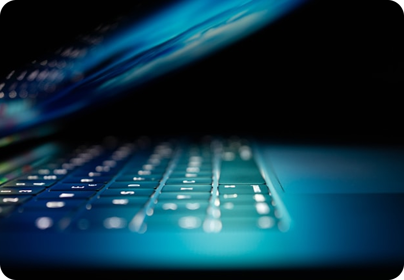 Close-up of a laptop keyboard glowing blue in a darkened room