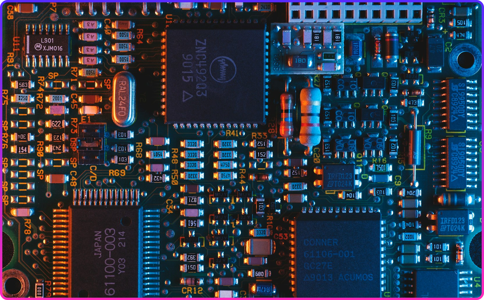 Macro shot of a circuit board's chips, resistors and solder joints lit in orange and blue