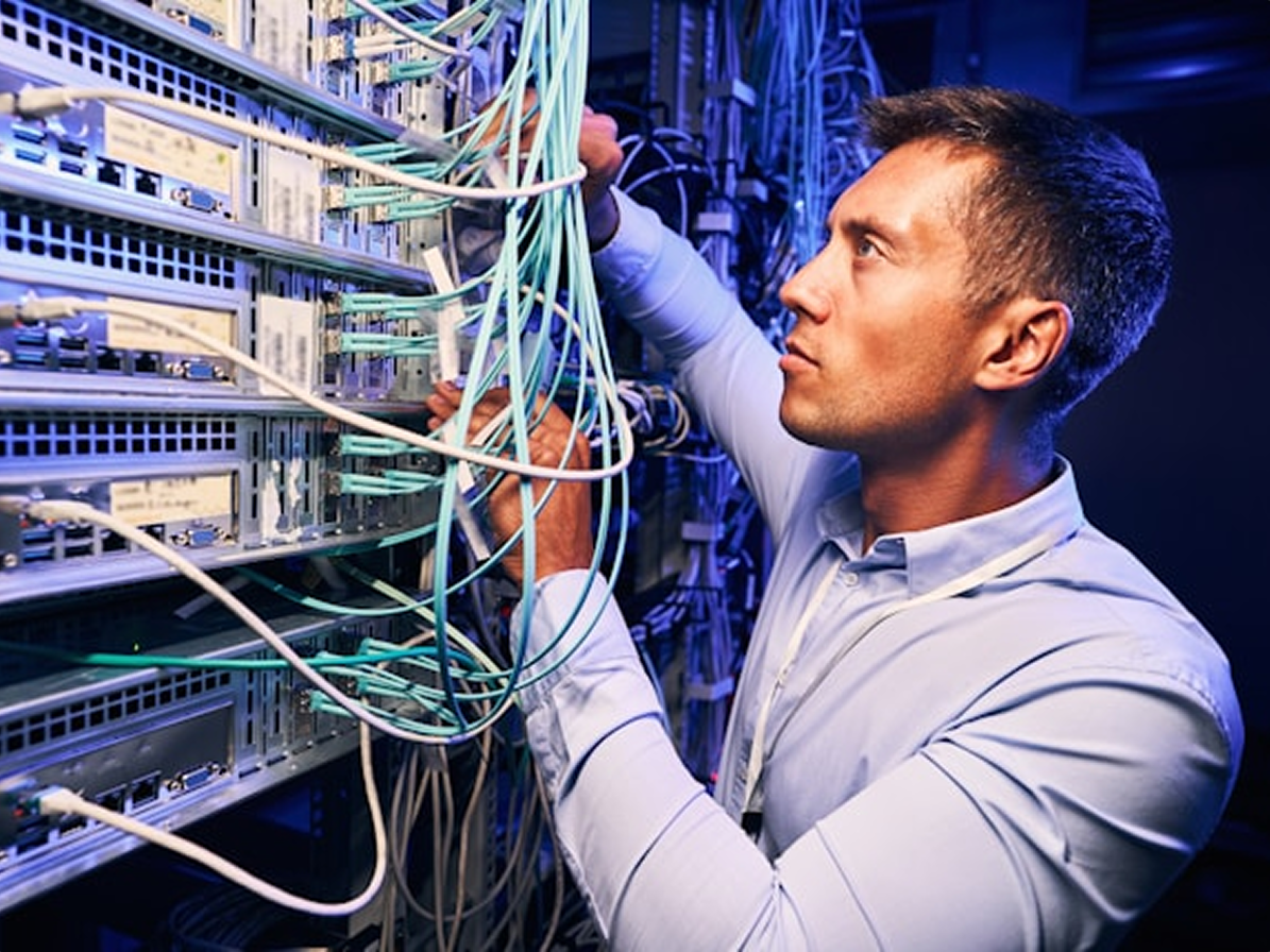 A technician in a data centre threading teal fiber optic cables into a server rack
