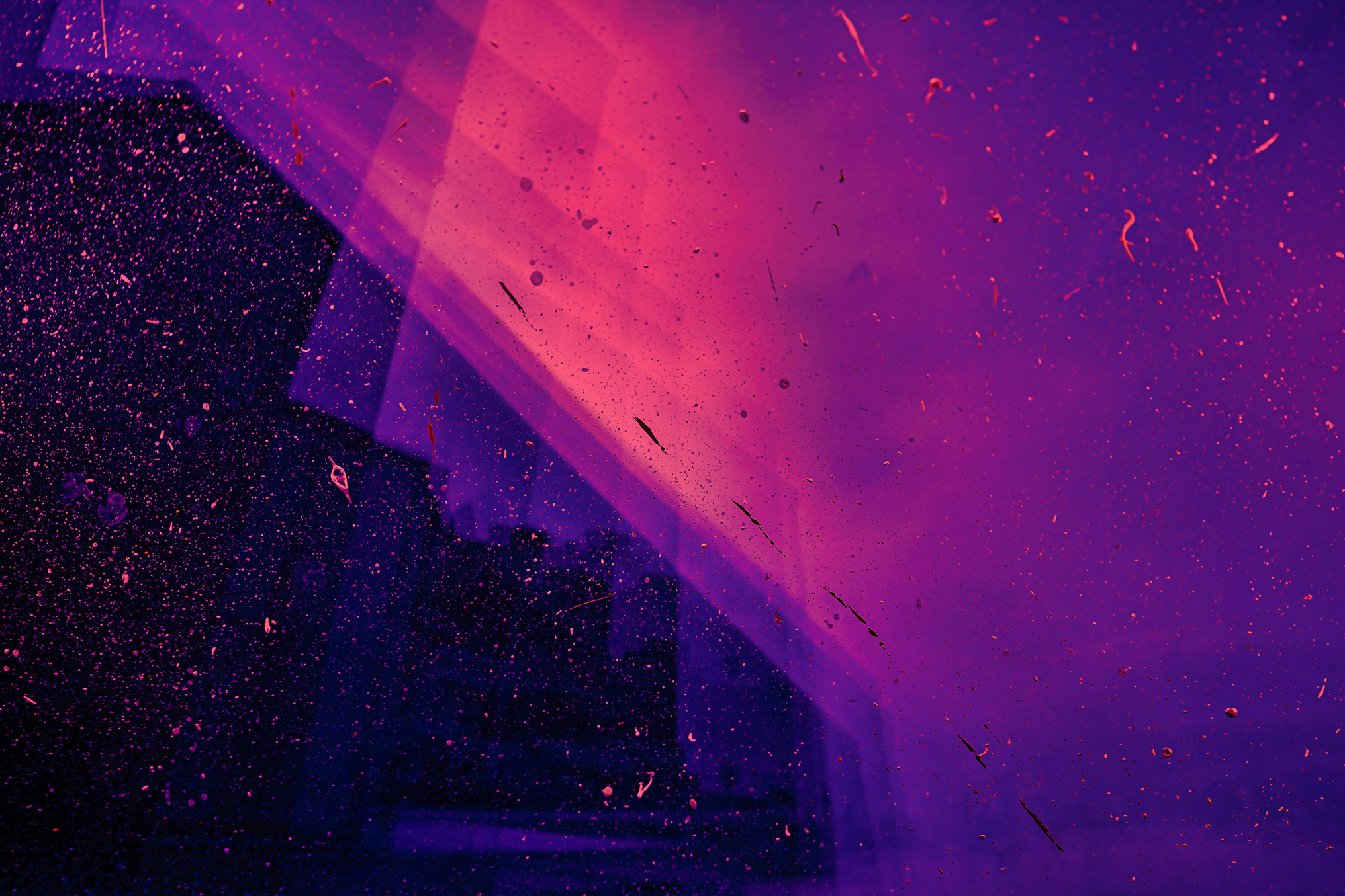 Streaks of pink and purple light falling across a dark, dust-speckled pane of glass